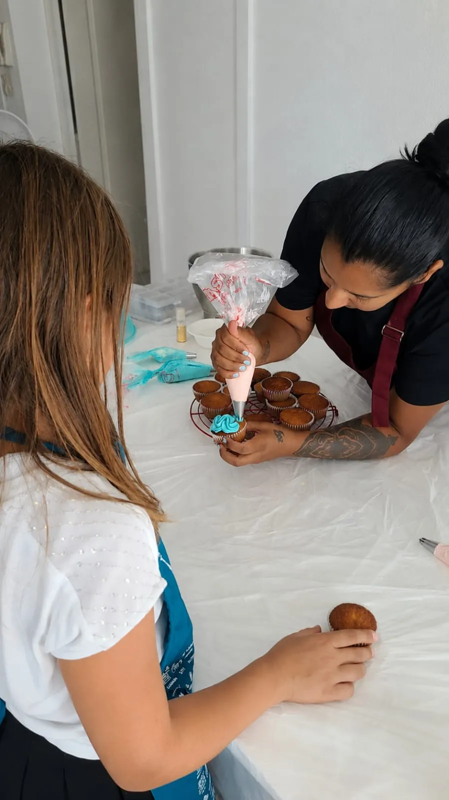 Sarah aide une enfant à pocher un glaçage bleu sur un cupcake