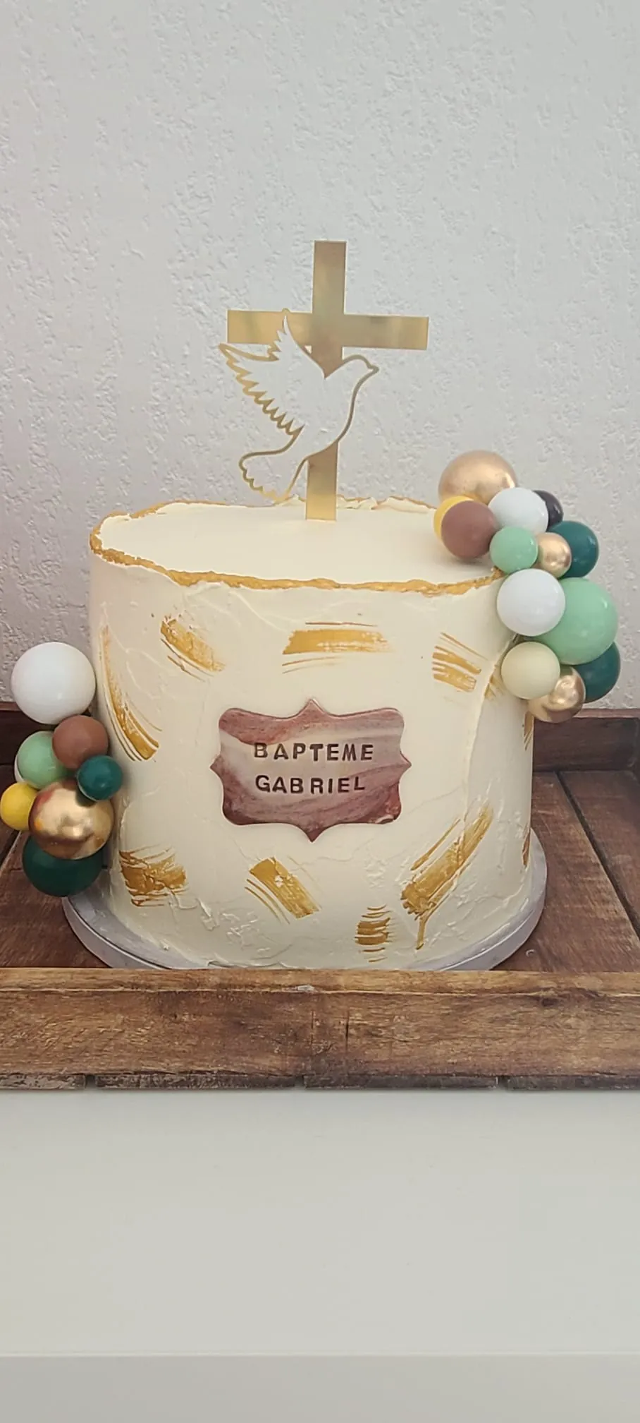 Layer cake ivoire à touches dorées, plaque "Baptême Gabriel" et décorations pastel