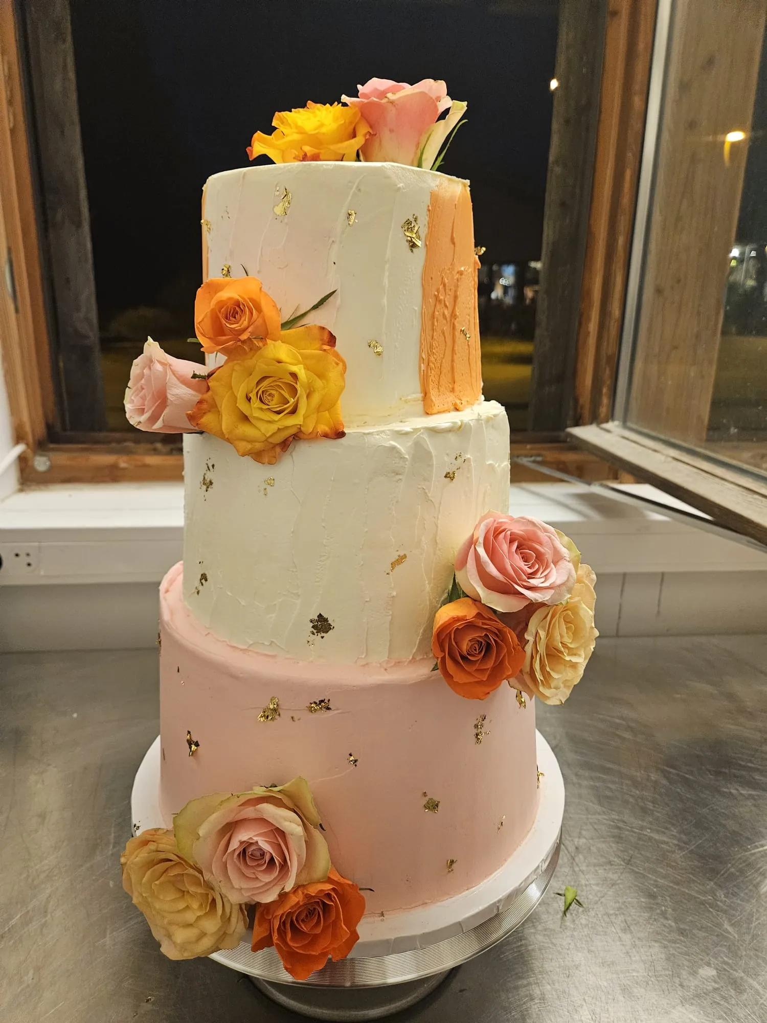 Wedding cake blanc à trois étages devant une fenêtre, roses fraîches