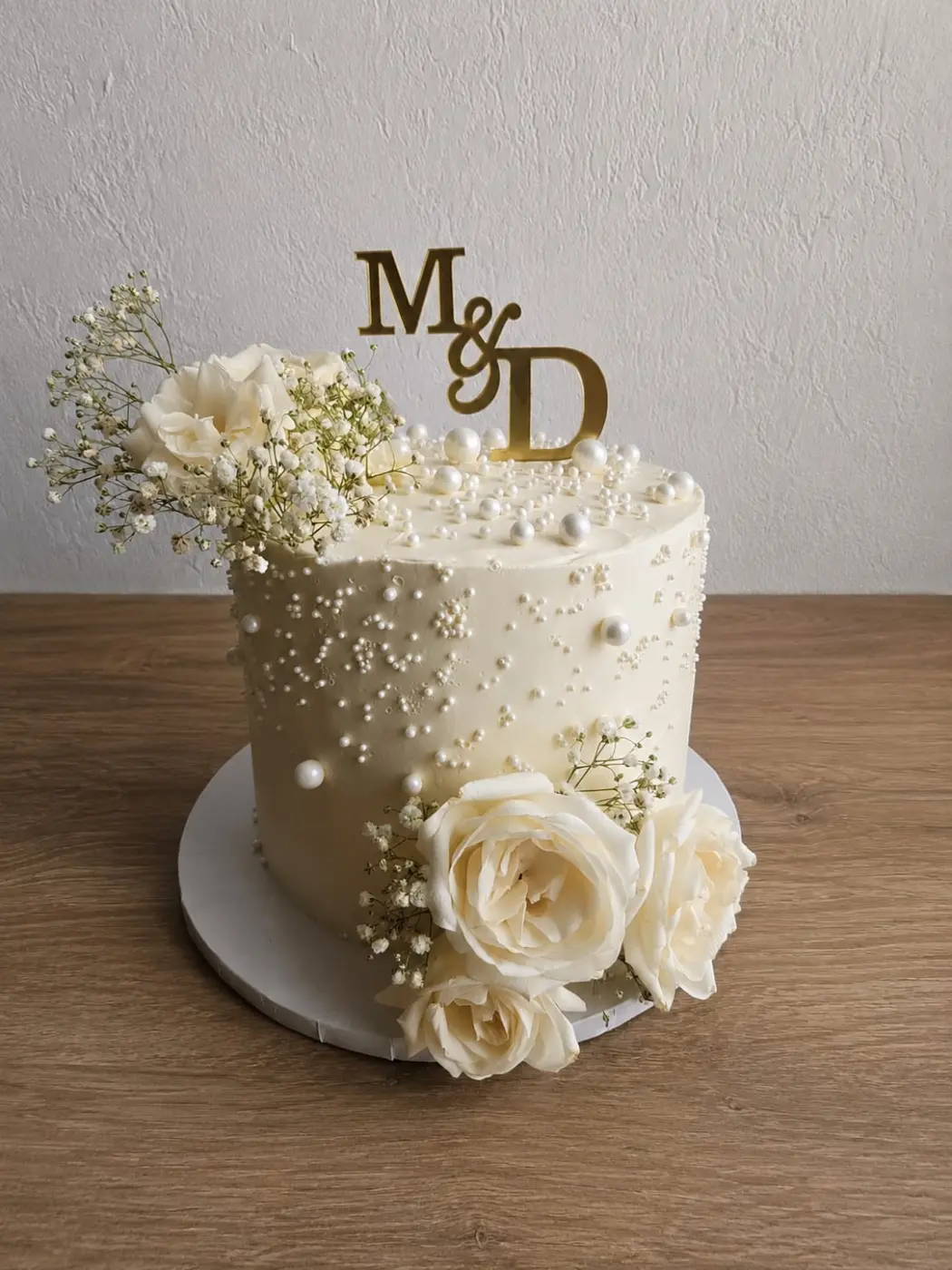Wedding cake ivoire à perles de sucre, roses blanches et gypsophile fraîches, topper doré "M & D"